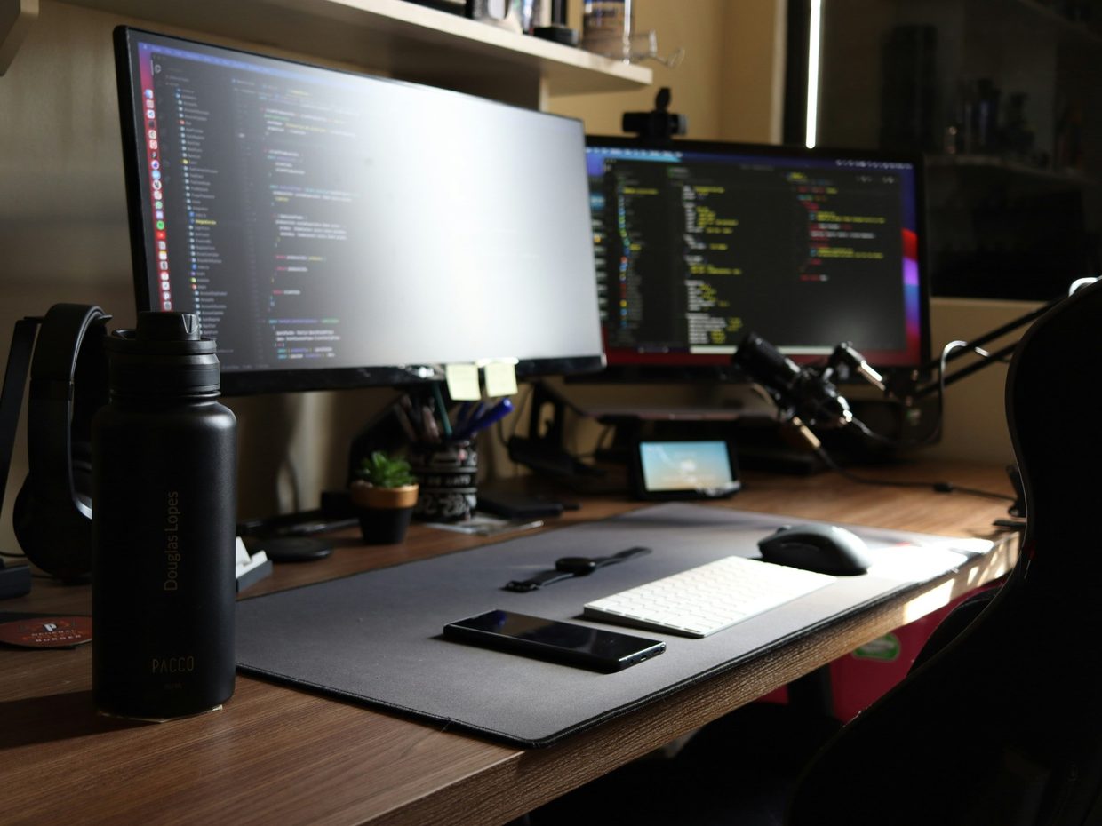 Poste de travail : deux écrans affichant du code, clavier et souris posés sur un bureau en bois.
